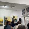 A picture taken at an art gallery featuring multiple pieces of art work and a busy atmosphere. 