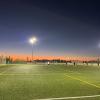 The final light from the sunset glows behind the green soccer field, full of players in the middle of a game.