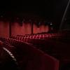 Dimly lit movie theater with red velvet seating and red curtains adorning the walls. 