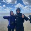 Two students smile and thumbs up for the camera, standing in the ocean