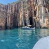 small boat floats in clear blue water and wall of reddish rocks behind it 