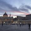 A view of St. Peter’s Basilica and St. Peter’s Square at sunset, with the basilica being illuminated by warm lights. 