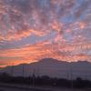 Vibrant oranges spread across the horizon and puffy clouds scatter the sky, the dark silhouette of the Andes mountains is a stark contrast to the colors.