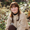Anja Caverley-Light smiling while sitting in a field of grass and flowers.