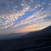 Soft yellows, warm oranges, and pale blues illuminate the cloud-filled sky behind misty silhouettes of mountains 