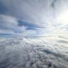 A wide shot of a blue sky covered in white clouds from the window of an airplane.