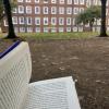 Open book in public garden with brick building and trees in background