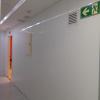 White hallway in a modern building. The corridor has smooth white walls and a white ceiling with recessed lighting running along it. 