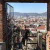 The author leans against a railing above a view of Graz, Austria, with many old buildings below. The photo is framed on both sides with brick pillars.