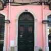 A pastel pink building facade with an arched doorway and two windows in Lisbon, Portugal