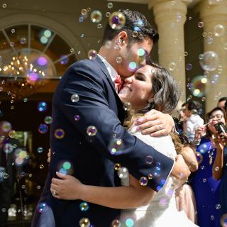 Justin and Monica at their wedding surrounded by guests blowing bubbles
