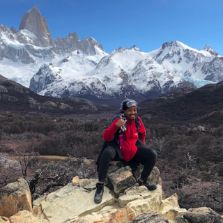 student in backpacking gear in front of snow capped mountains