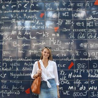 a girl standing near the wall with text and looking at the camera person 