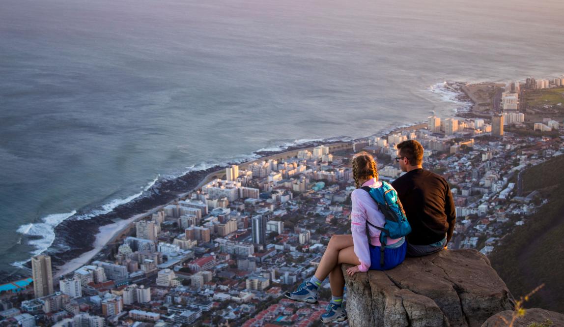 two students sit on the edge of a mountain above Cape Town's city and coast line