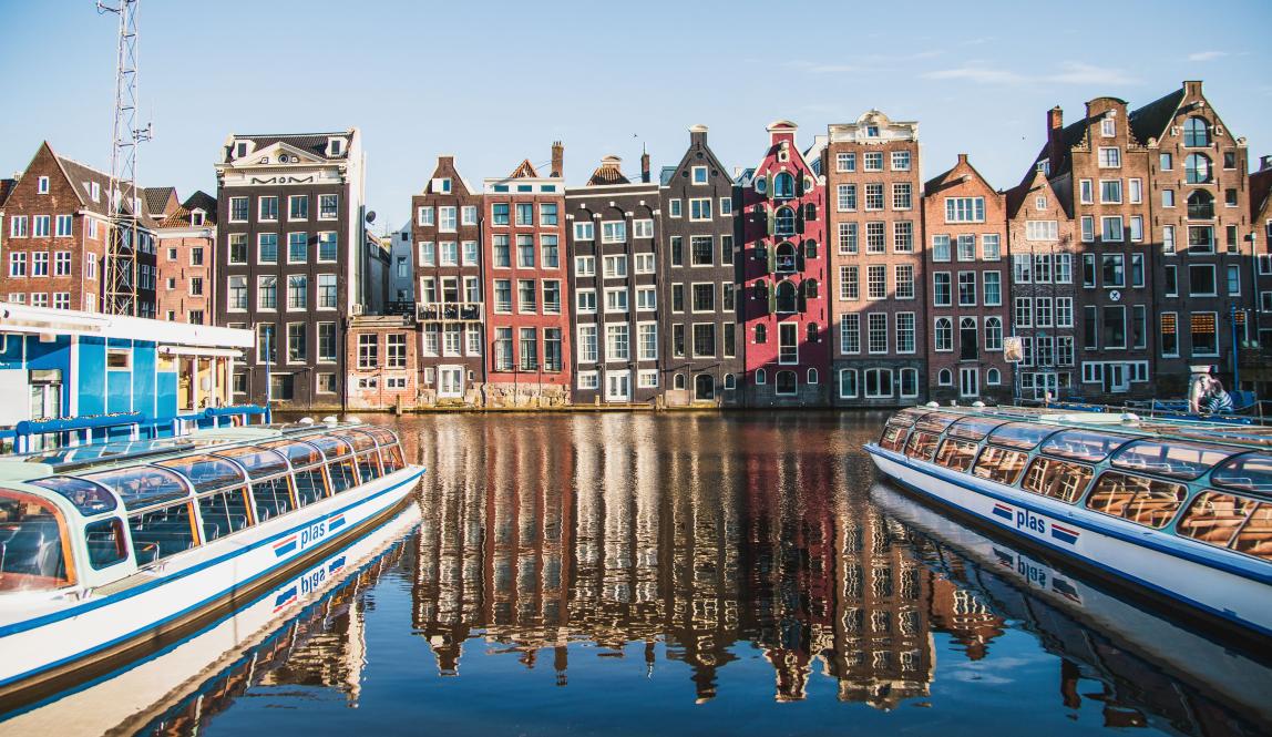 boats sit in Amsterdam Centraal Canal in front of traditional Amsterdam architecture