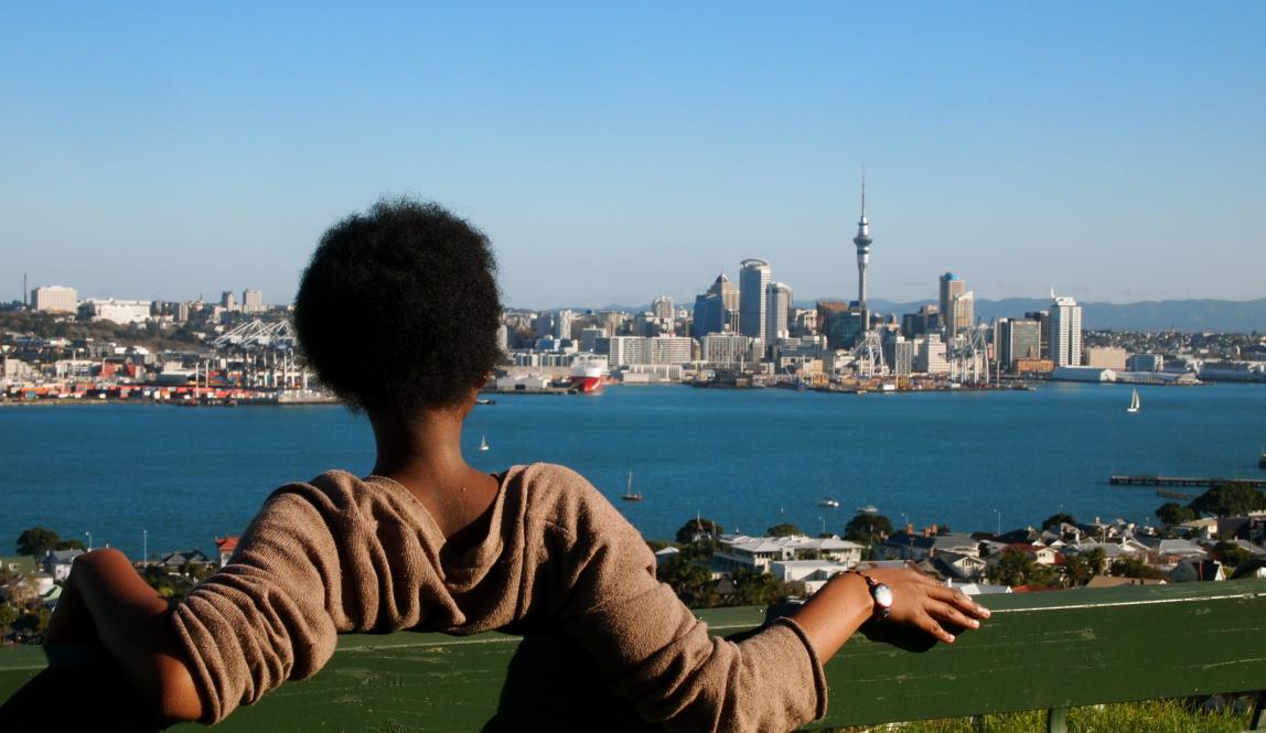 a student sitting on a bench at the top of Mount Victoria, looking at the Auckland skyline