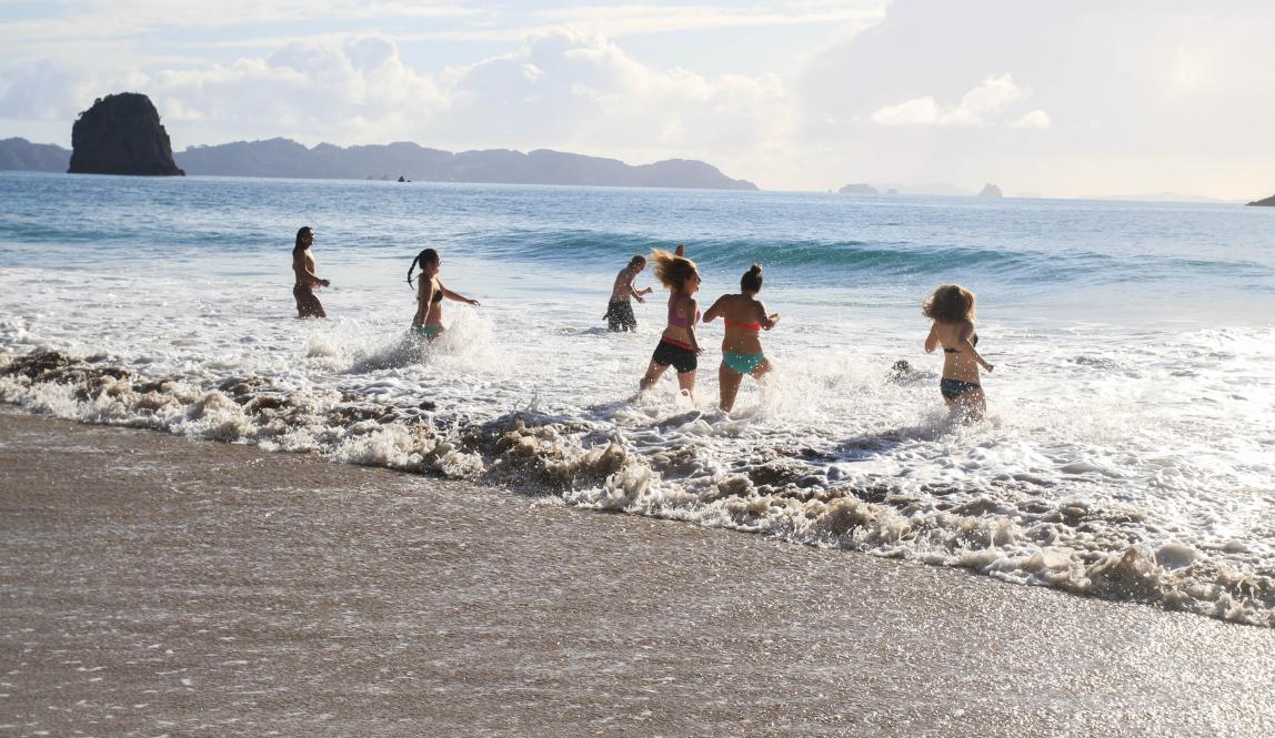 a group of students run into the water at Cathedral Cove
