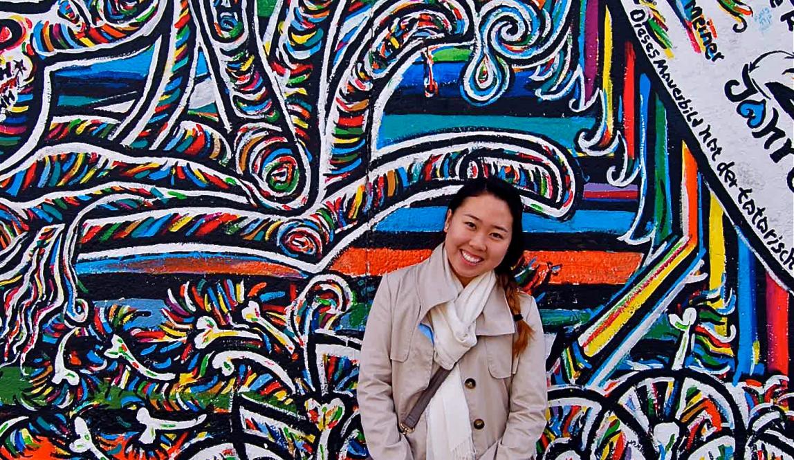 a student poses in front of the Berlin Wall