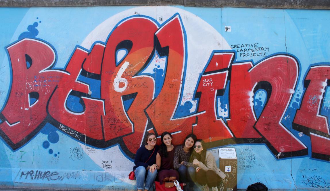 a group of students pose for a photo in front of a Berlin mural on the Berlin Wall