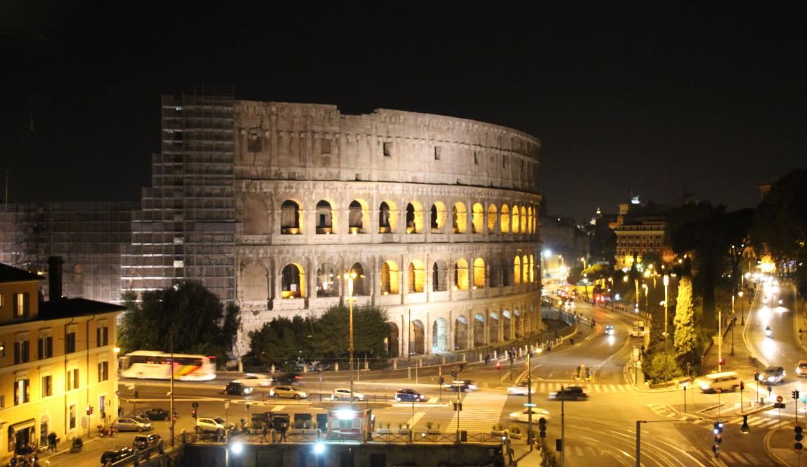 Colosseum illuminated at night, with surrounding city lights. This alt text was added with Al; accuracy may vary.