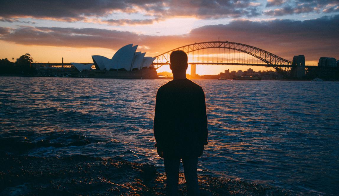 an artistic shot of a student looking at Sydney Opera House and Bridge at sunset