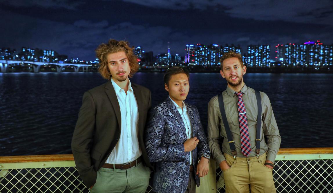 three students pose for a photo in front of the Seoul skyline at night
