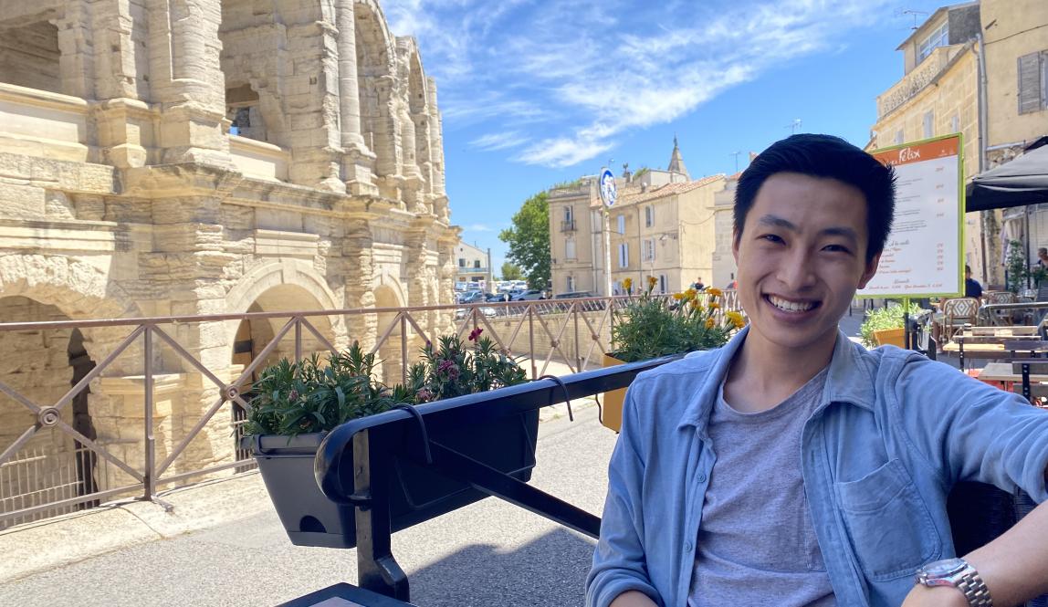 a student smiles for a photo while at an outdoor cafe by Les Arenas in Arles
