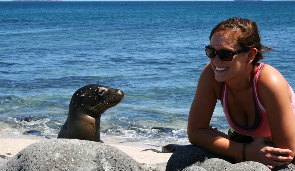 a student poses for a photo with a Galápagos sea lion on the beach