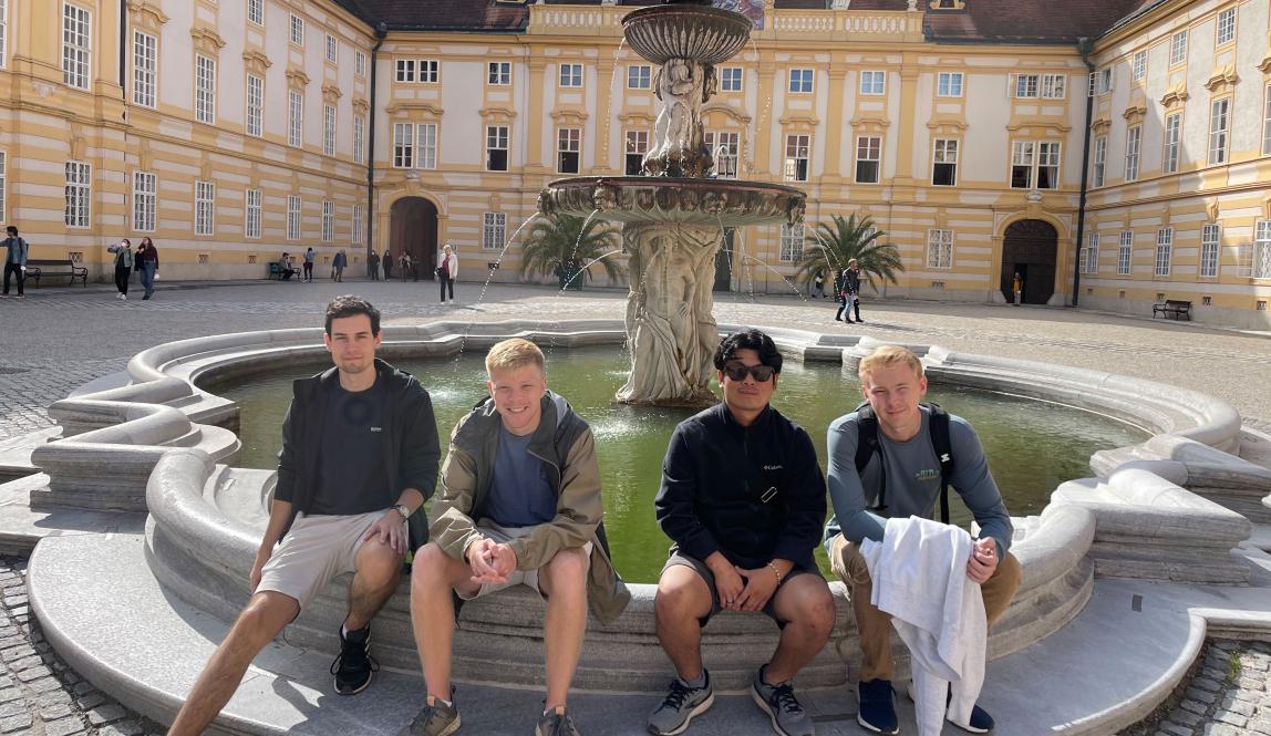 four students pose for a photo at Melk Abbey while sitting on the edge of the fountain
