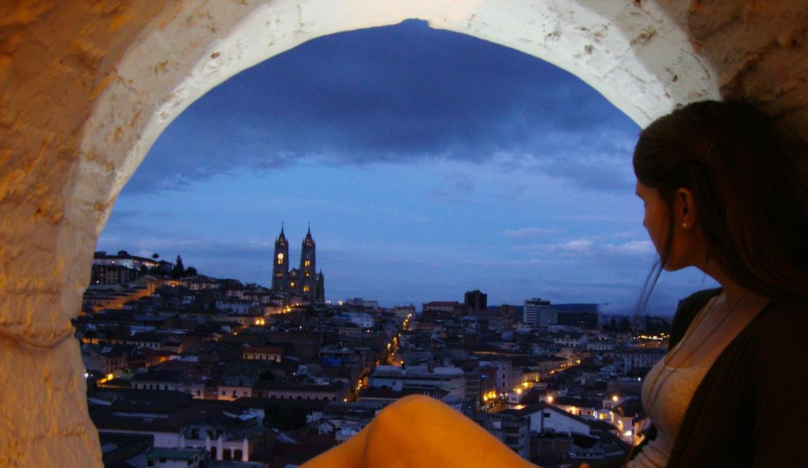 a student sits in a window in Quito overlooking the city and Basílica del Voto Nacional