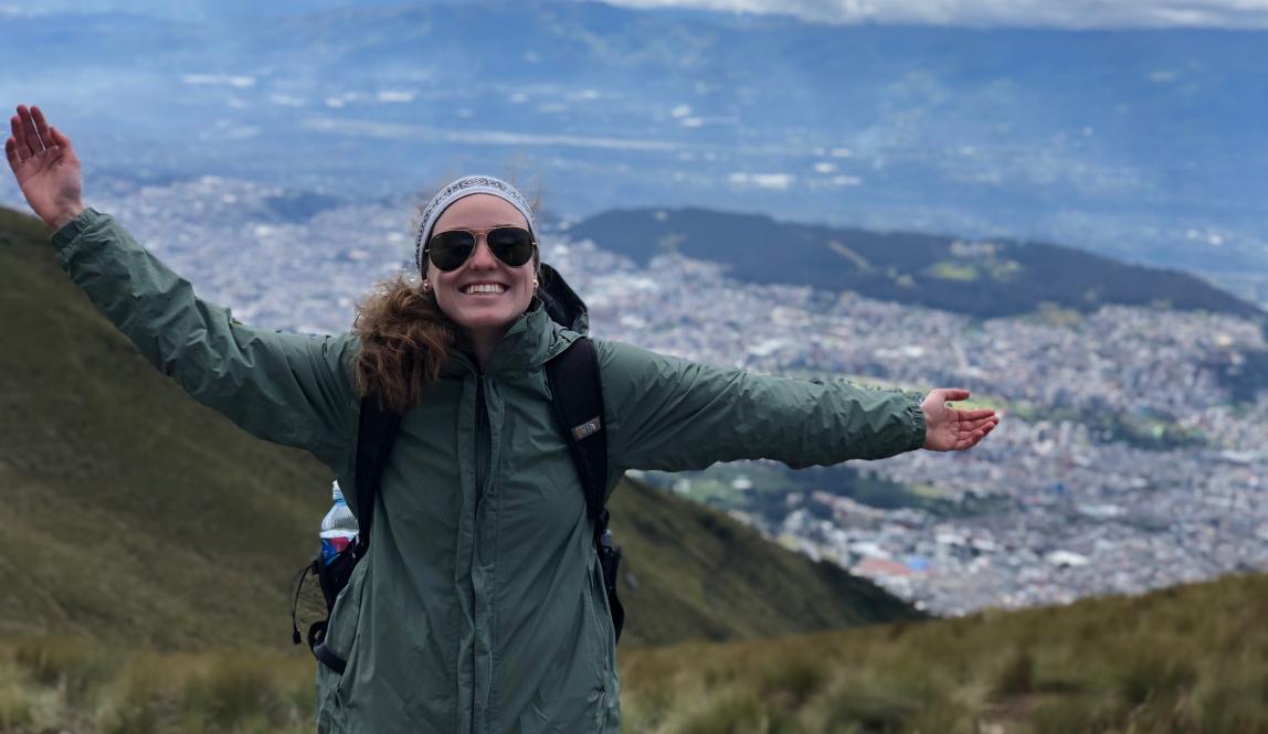 a student poses for a photo from atop the mountains in Quito with a backdrop of the city