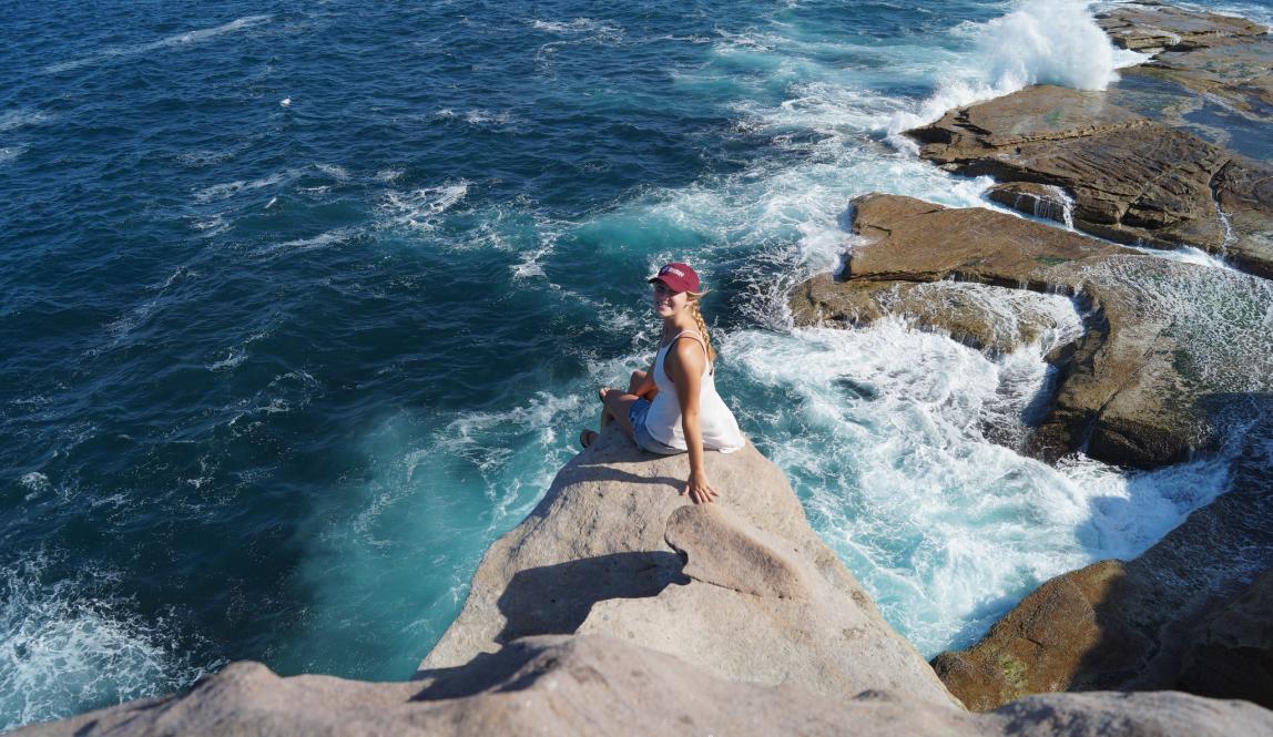 a student poses for a photo on a seaside rock in Sydney