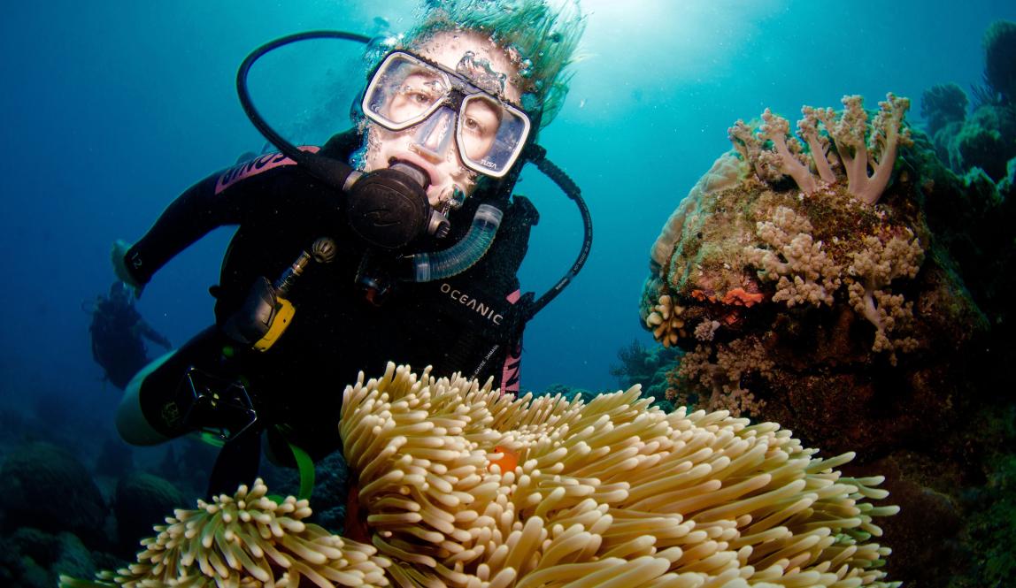 a student poses for a photo with an anemone while scuba diving at the Great Barrier Reef