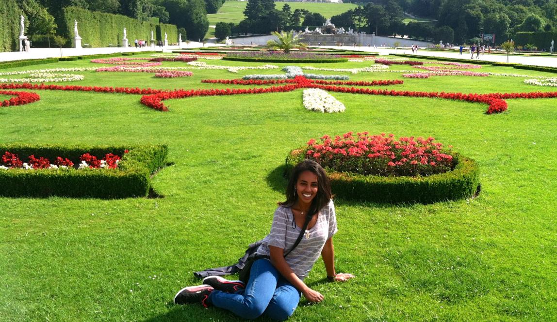 a student posing for a photo while sitting on the ground at Schönbrunn Palace in Vienna on a sunny day among flowers