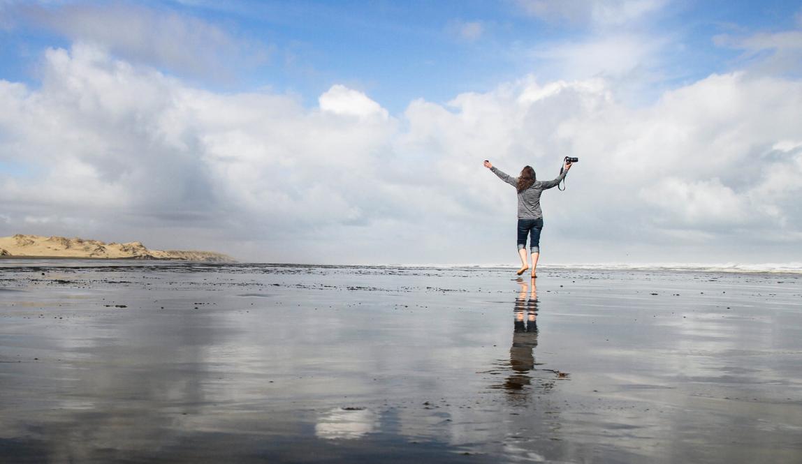 a student holding a DSLR camera in the air while walking on 90 Mile Beach in New Zealand