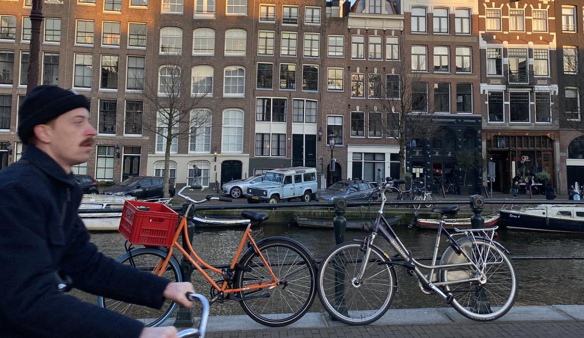 a man riding by on a bike in front of buildings in Amsterdam