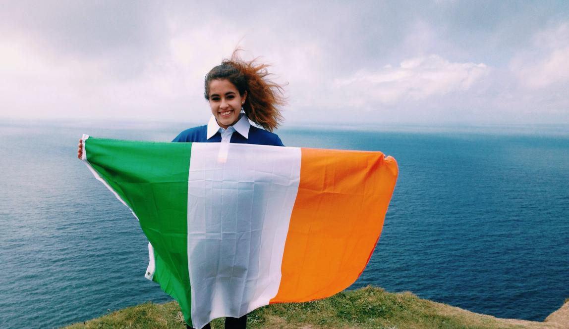 a student holding an Irish flag at the Cliffs of Moher