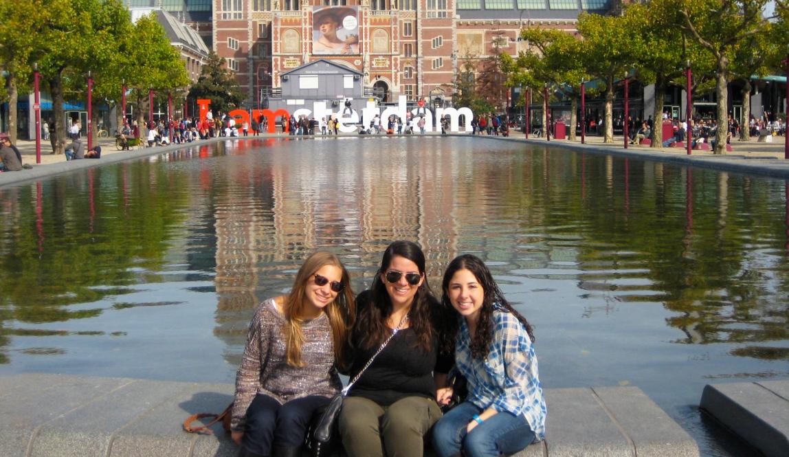 three students sitting in front of the I Amsterdam sign