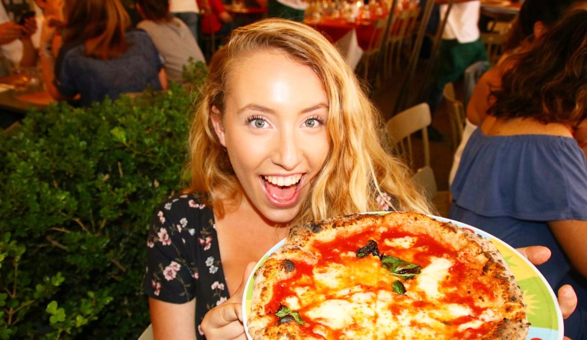 a student posing for a photo with her pizza in Italy