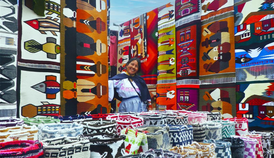 a seller at the market in Otavalo surrounded by colorful quilts