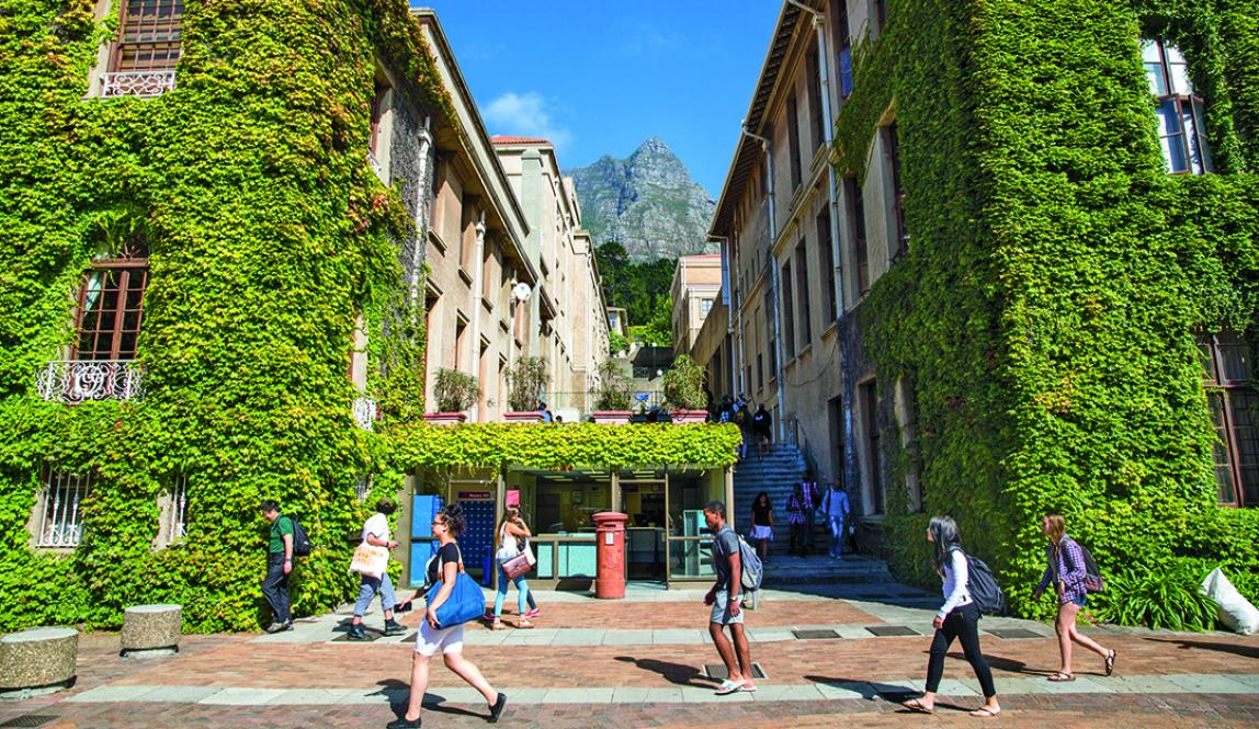 Students walk past buildings covered in lush vegetation on a sunny day at the University of Cape Town.