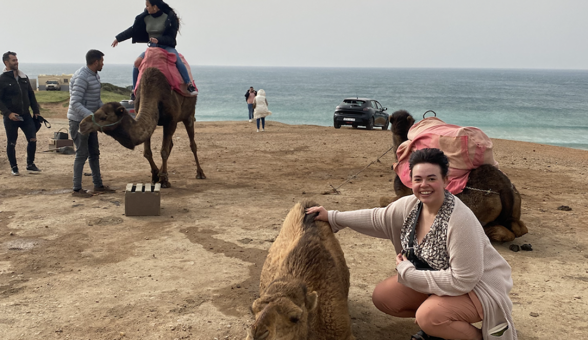 A woman petting a camel with the sea in the background