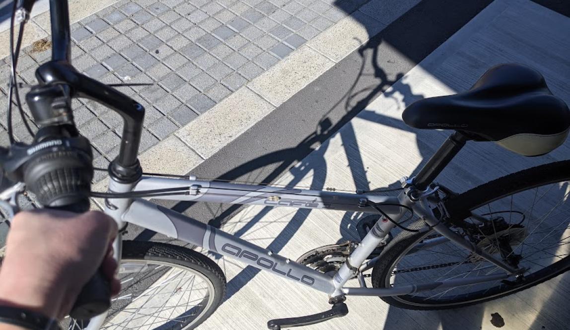 Image of a hand holding the handlebars of a silver bike with a black seat. 