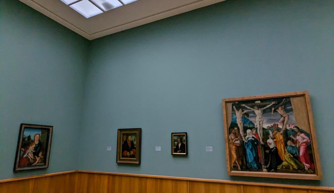 Corner of empty room in art museum with 4 paintings hanging on the walls.