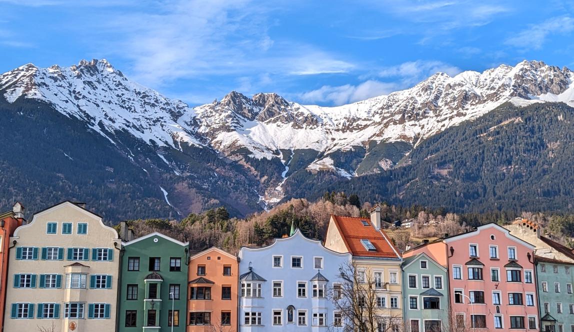 Colorful houses lining a river with mountains capped with snow in the background.