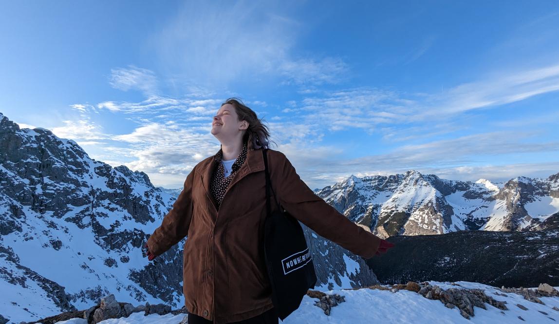 Person with arms stretched out with Alps in the background.