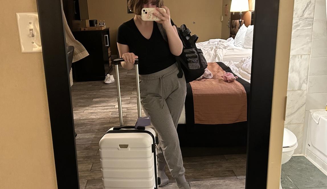 A photo of me in the mirror holding my suitcase and personal item in my hotel room.