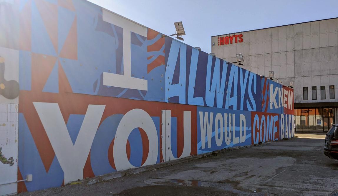 Large mural in white, blue, and red saying "I Always Knew You Would Come Back"