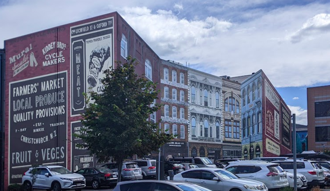 A mural of multiple buildings pasted onto the flat side of a building, creating the illusion of 3D buildings. 