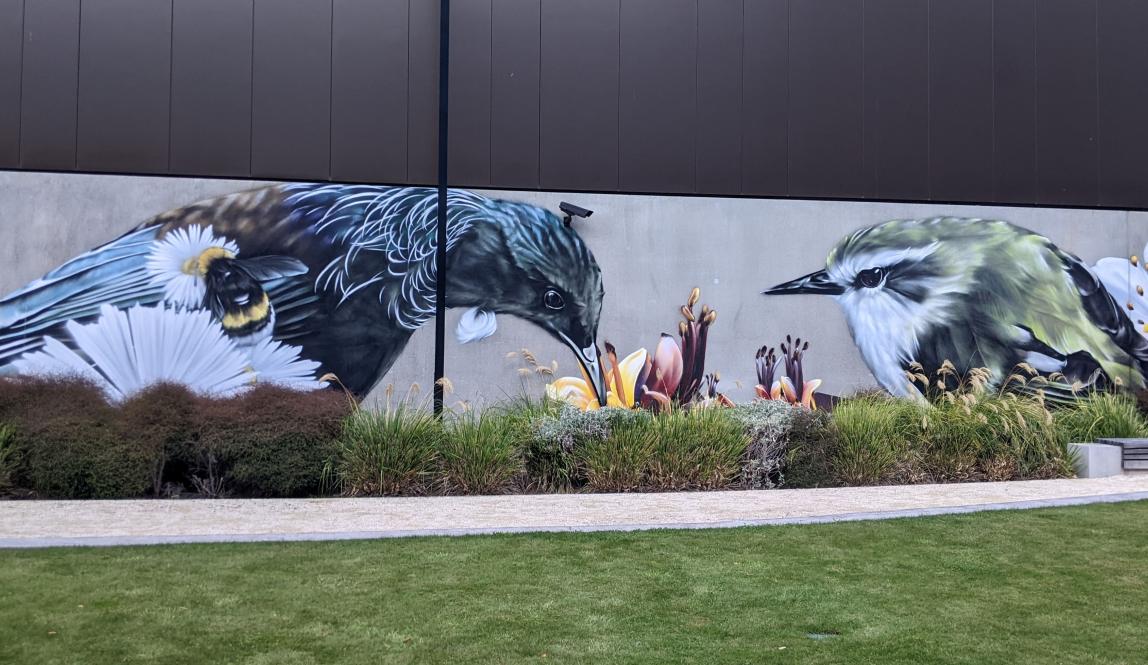 Mural of two birds, a Tui and a Silvereye, consuming flower nectar next to a bumblebee